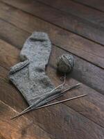 Hand gestrickt Socke mit Nadeln und grau Garn Ball auf dunkel hölzern Hintergrund. foto