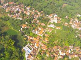 Vogel Auge Aussicht von Dorf unter Reis Felder im bandung Stadt, Indonesien. Landschaft von Ackerland mit Reis Terrasse landwirtschaftlich Pflanzen im Landschaft. landwirtschaftlich Feld. über. Schuss von ein Drohne fliegend foto