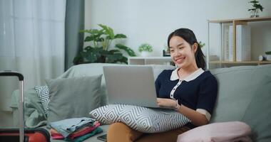 Porträt von asiatisch Teenager Frau Sitzung auf Sofa mit Laptop zum bereiten Buchung Hotel und Flugzeug Fahrkarte zum Reise. Backpacker Reise Konzept. foto