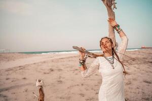 Modell- im Boho Stil im ein Weiß lange Kleid und Silber Schmuck auf das Strand. ihr Haar ist geflochten, und Dort sind viele Armbänder auf ihr Waffen. foto