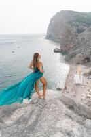 Frau Meer Grün Kleid. Seite Aussicht ein glücklich Frau mit lange Haar im ein lange Minze Kleid posieren auf ein Strand mit Ruhe Meer Bokeh Beleuchtung auf sonnig Tag. Mädchen auf das Natur auf Blau Himmel Hintergrund. foto