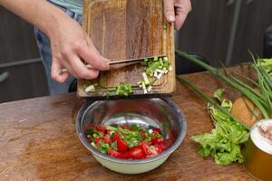 hacken das Grün Zwiebeln und Tomaten und Platz Sie im ein Schüssel. bereiten das Salat. foto