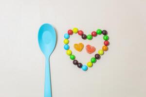 Herz geformt Süßigkeiten und multi farbig Süßigkeiten und Blau Löffel auf isoliert auf Weiß Hintergrund. foto