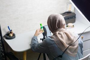 Frau mit Hijab ist Arbeiten mit Handy, Mobiltelefon Telefon zu machen ein und produzieren Inhalt zum Verkauf Produkt foto