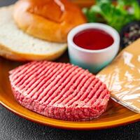 Burger einstellen roh Kotelett, Brötchen, Käse, Tomate Soße, Grüns frisch Kochen Vorspeise Mahlzeit Essen Snack auf das Tabelle Kopieren Raum Essen Hintergrund rustikal foto