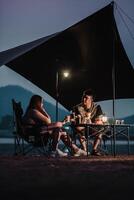 Paar engagiert im ein tief Konversation beim ein Campingplatz, beleuchtet durch das Sanft glühen von Zelt Beleuchtung gegen das Nacht Himmel. foto