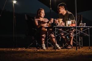 Paar genießt ein warm trinken und Konversation beim ihr friedlich Campingplatz unter Umgebungs Beleuchtung. foto