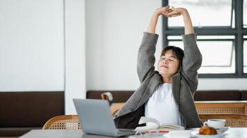 jung Freiberufler nimmt ein Moment zu strecken und entspannen während ein Arbeit brechen, Sitzung beim ein Cafe Tabelle mit ihr Laptop und Anmerkungen. foto