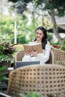 heiter Freiberufler nimmt Anmerkungen im ein Notizbuch, Arbeiten effizient mit ein Laptop im ein beschwingt Garten Einstellung. foto