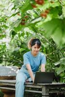 konzentriert jung Frau einnehmend im freiberuflich Arbeit auf ihr Laptop inmitten das natürlich Umfeld von ein Garten Bank. foto