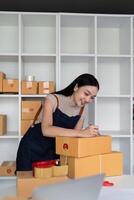 Frau asiatisch im ein online Geschäft prüfen das Kunde Adresse und schreiben das Information auf das Kasten. online Einkaufen Konzept foto