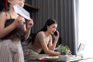 asiatisch Geschäft Frau Arbeit beim Zuhause mit jung Kind Tochter abspielen um. Mutter Verlust Konzentration auf Job im Laptop Computer und Gefühl frustriert von Kinder Herstellung Lärm im Haus foto