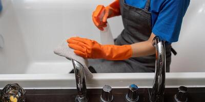 Fachmann Reinigung Bedienung Unternehmen Mitarbeiter im Gummi Handschuhe Reinigung und Waschmittel sprühen im Badezimmer foto