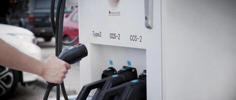 Hand halten ev Laden Stecker im Vorderseite von Kamera mit verschwommen Hintergrund von draussen. Treiber von elektrisch Auto halt Batterien Ladegerät Stecker. nachhaltig Energie angetrieben elektrisch Laden Bahnhof Hintergrund foto