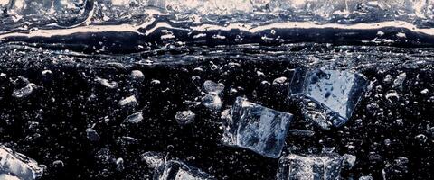 Wasser planschen und Eis Würfel. Eis planschen in ein Glas von Wasser. unter Wasser Gießen Eis Würfel fallen in klar Bewässerung Hintergrund. erfrischend Ausruhen Trinken. Eis im ein Glas mit Blau Hintergrund foto