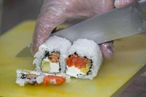 ein behandschuhte Hand schneidet Sushi auf ein Schneiden Tafel. foto