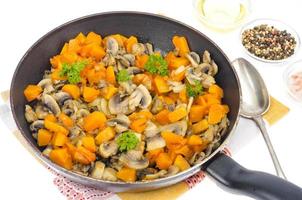 Vegetarischer Gemüseeintopf aus Kürbis und Pilzen in der Pfanne, weißer Hintergrund.