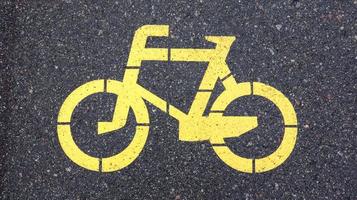 Fahrradsymbol, das einen Weg für Fahrräder darstellt. gelb lackiertes Schild für Fahrräder auf dem Asphalt. flach, Ansicht von oben. foto