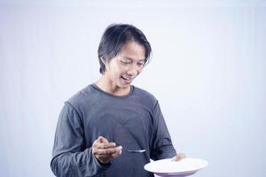 asiatisch Mann zeigen gegenüber leeren Teller mit glücklich Ausdruck isoliert Weiß Hintergrund zum Kaffee Foto Raum. Essen Speisekarte Präsentation Konzept.