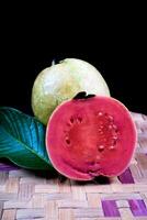 Guave isoliert. Sammlung von rot fleischig Guave Obst mit gelblich Grün Haut und Blätter isoliert auf schwarz Hintergrund mit gewebte Bambus. foto