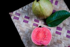 Guave isoliert. Sammlung von rot fleischig Guave Obst mit gelblich Grün Haut und Blätter isoliert auf schwarz Hintergrund mit gewebte Bambus. foto