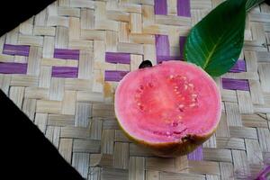 Guave isoliert. Guave Obst mit rot Fleisch mit gelblich Grün Haut und Blätter isoliert auf ein schwarz Hintergrund mit gewebte Bambus wie ein Base. foto