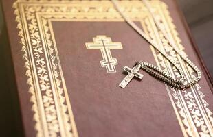 Silberhalskette mit Kruzifixkreuz auf christlichem Bibelbuch auf schwarzem Holztisch. Gott um Segen bitten mit der Kraft der Heiligkeit, die Glück bringt foto
