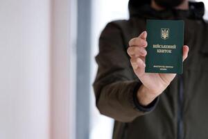 jung ukrainisch Wehrpflichtiger Soldat zeigt an seine Militär- Zeichen oder Heer Ich würde Fahrkarte drinnen foto