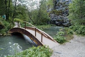 das alt hölzern Brücke von das gewölbt Art geht vorbei durch ein Berg Strom, ein Geländer auf das Brücke, ein natürlich Park, das Fluss Schulgen Kapova Höhle. foto