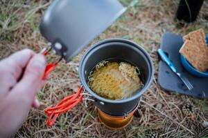 Tourist Utensilien, Lager Kochen im ein Topf, öffnen das Deckel aussehen Innerhalb das Topf, Koch Nudeln, ein schnell Mahlzeit im Natur, Mittagessen im das Wald auf das Gras, Trekking im das Berge foto