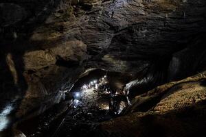 das Stein Gewölbe von das Höhle, das Licht leuchtet das Decke von das Karst Höhle, ein Gruppe von Menschen gehen zu prüfen das Gips Höhle, ein Riese unter Tage Passage. foto