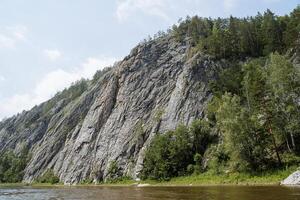 felsig Berge absteigen in das Fluss, bergig Terrain, Taiga Fluss, Panorama Berg Fluss, steil Cliff, Grün Wald Landschaft Hügel. foto