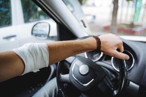 das Kerl sitzt hinter das Rad von das Auto, das verletzt Hand Lügen auf das Lenkung Rad, das Ellbogen tut weh, das Joint ist verbunden, das des Mannes Hand ist im das Wagen. foto