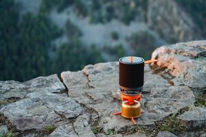 Tourist Utensilien Bowler Stehen auf das Kante von ein Felsen Felsen, Camping Gas zum Kochen auf ein Wanderung, kompakt Ausrüstung zum Bergsteigen. foto