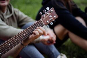 das Kerl Theaterstücke das Gitarre im das Wald, das Lieder um das Feuer, das Finger von das Hand Klemme das Saiten auf das Griffbrett, das Griffbrett von das Gitarre mit das Saiten. foto