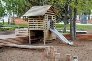 ein hölzern Kinder- Haus mit ein gleiten, ein Sport Spielplatz, ein Platz zum Kinder zu spielen, ein rutschen Fahrt, ein modern Amüsement Park, ein Kindergarten auf das Straße. foto