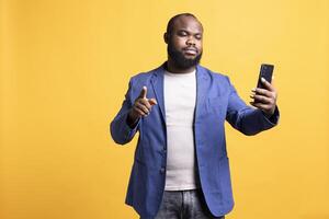 ärgerlich afrikanisch amerikanisch Mann Kampf mit freunde während Konferenz Treffen mit Handy, isoliert Über Studio Hintergrund. empört Person streiten mit Kumpels während Internet Anruf foto