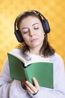 optimistisch Frau drehen Seite auf Buch und Hören Musik, vermitteln Freude von lesen Konzept, Studio Hintergrund. Geek lesen Roman und Hören Lieder im Kopfhörer, zeigen Anerkennung zum Literatur foto