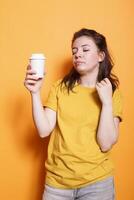 müde Frau posieren gegen isoliert Orange Hintergrund im beiläufig Kleidung, halten Kaffee Tasse, entspannend mit geschlossen Augen. schläfrig Ausdruck von jung Brünette Dame zeigt Erschöpfung und Müdigkeit. foto