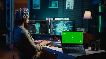 Ingenieur mit eeg Headset auf Programmierung Gehirn Transfer in Computer virtuell Welt Nächster zu Grün Bildschirm Laptop. transhumanistisch mit Neurowissenschaften zu dazugewinnen Digital Seele, Attrappe, Lehrmodell, Simulation Gerät, Kamera b foto