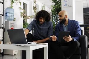 Unternehmer und Kollege diskutieren Projekt während Analysieren Daten auf Laptop im Geschäft Büro. arabisch Angestellte Planung Produkt Beförderung Strategie zusammen im Coworking Raum foto