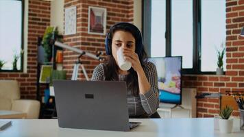 Telearbeiter Überprüfung E-Mails auf Laptop während beim Computer Schreibtisch, Trinken Kaffee und Hören Musik. Fernbedienung Mitarbeiter mit Kopfhörer auf Arbeiten von Zuhause lösen Aufgaben, genießen heiß Getränk, Kamera ein foto