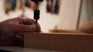 Holzarbeiter mit Leistung bohren zu erstellen Löcher zum Dübel im hölzern Planke, schließen hoch. Zimmermann sinkt Schrauben in hölzern Oberflächen mit elektrisch Werkzeug, tun präzise Bohren zum nahtlos Tischlerei, Kamera ein foto