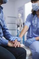 Nahansicht von weiblich Krankenschwester halten Hände von Senior geduldig beim Krankenhaus Büro. medizinisch Praktiker tragen Handschuhe hilft im Ruhestand alt Mann nach ein Chiropraktik Untersuchung und Diagnose. foto
