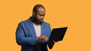 afrikanisch amerikanisch Mann mit Laptop zu tun Geschäft verbunden Aufgaben zum Unternehmen, isoliert Über Studio Hintergrund. Büro Verkäufer tun Budgetierung, Prognose, und finanziell Analyse auf Notizbuch, Kamera ein foto