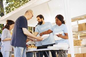 gemischtrassig Mannschaft Arbeiten zusammen beim Essen Antrieb, wohltätig verteilen wesentlich Artikel zu weniger glücklich. multiethnisch Menschen tragen Blau T-Shirts Bereitstellung Hunger Linderung und Freiwillige Hilfe. foto