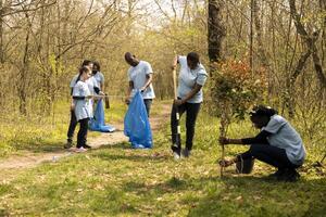 Gruppe von vielfältig Freiwillige pflücken oben das Müll und Plastik Abfall, Sammeln und Recycling Müll im das Wald Bereich. Aktivisten tun freiwillig Arbeit zu sauber das natürlich Umfeld. foto