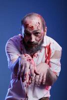 Porträt von Mann gekleidet wie schrecklich gruselig Zombie bedeckt im Blut zum Halloween Party. Person tragen unheimlich bilden, vorgeben zu Sein Untote Monster- mit Narben, Studio Hintergrund foto