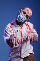 Porträt von Darsteller spielen Zombie im Grusel Film tragen Gesicht Maske während Coronavirus Ausbruch. Mann gekleidet wie wiederbelebt Leiche zum bevorstehende Thriller Film, infiziert mit Covid, Studio Hintergrund foto