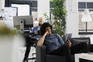 Start oben Geschäft Unternehmen Manager Aufpassen auf Digital Tablette während brechen im Büro. arabisch jung Unternehmer Surfen Sozial Medien und entspannend auf Couch im Coworking Raum foto